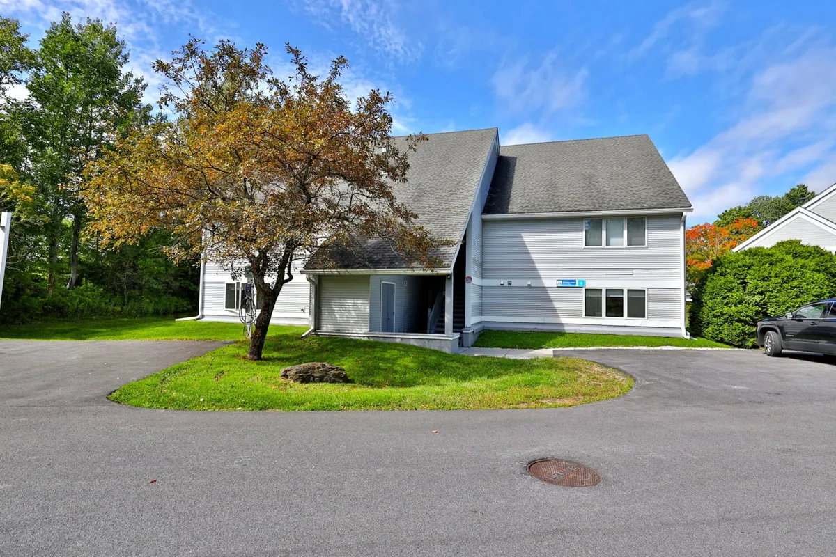 An exterior view of the building with a tree in the foreground, a driveway, and a welcoming facade. The outdoor space suggests a friendly environment suitable for sunny afternoons in the yard or small gatherings.