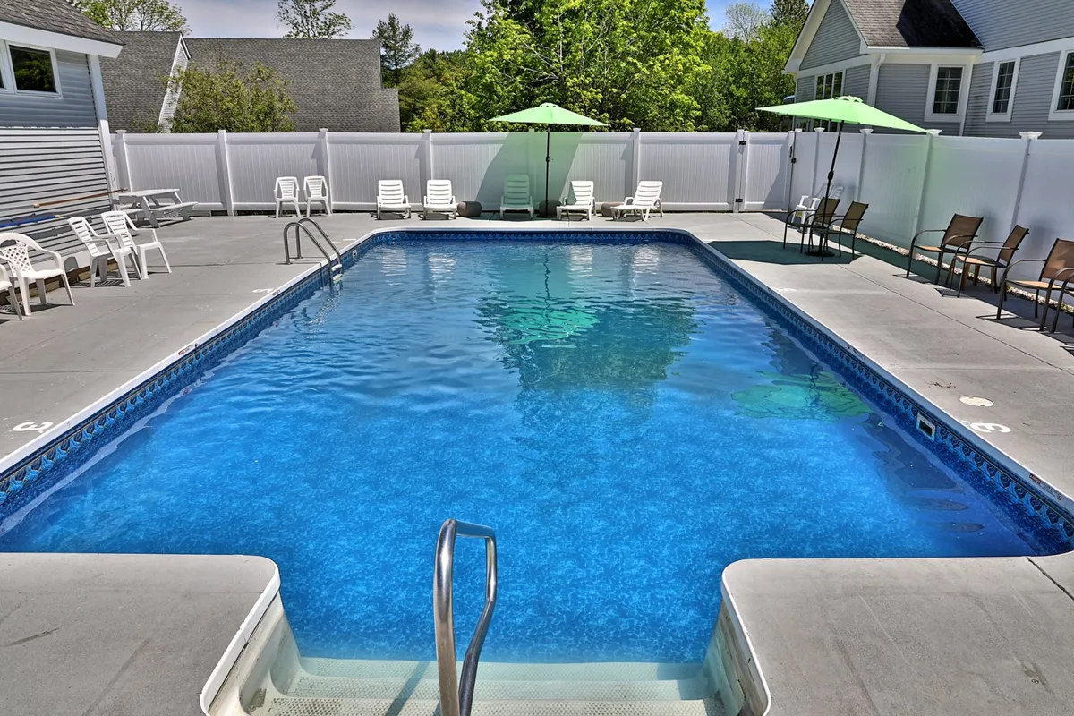This image captures a different angle of the swimming pool, focusing on the inviting blue water, lounge chairs neatly arranged around the perimeter, and several green umbrellas offering shade. The scene is set for sunset, suggesting an atmosphere of leisurely afternoons and evening gatherings.