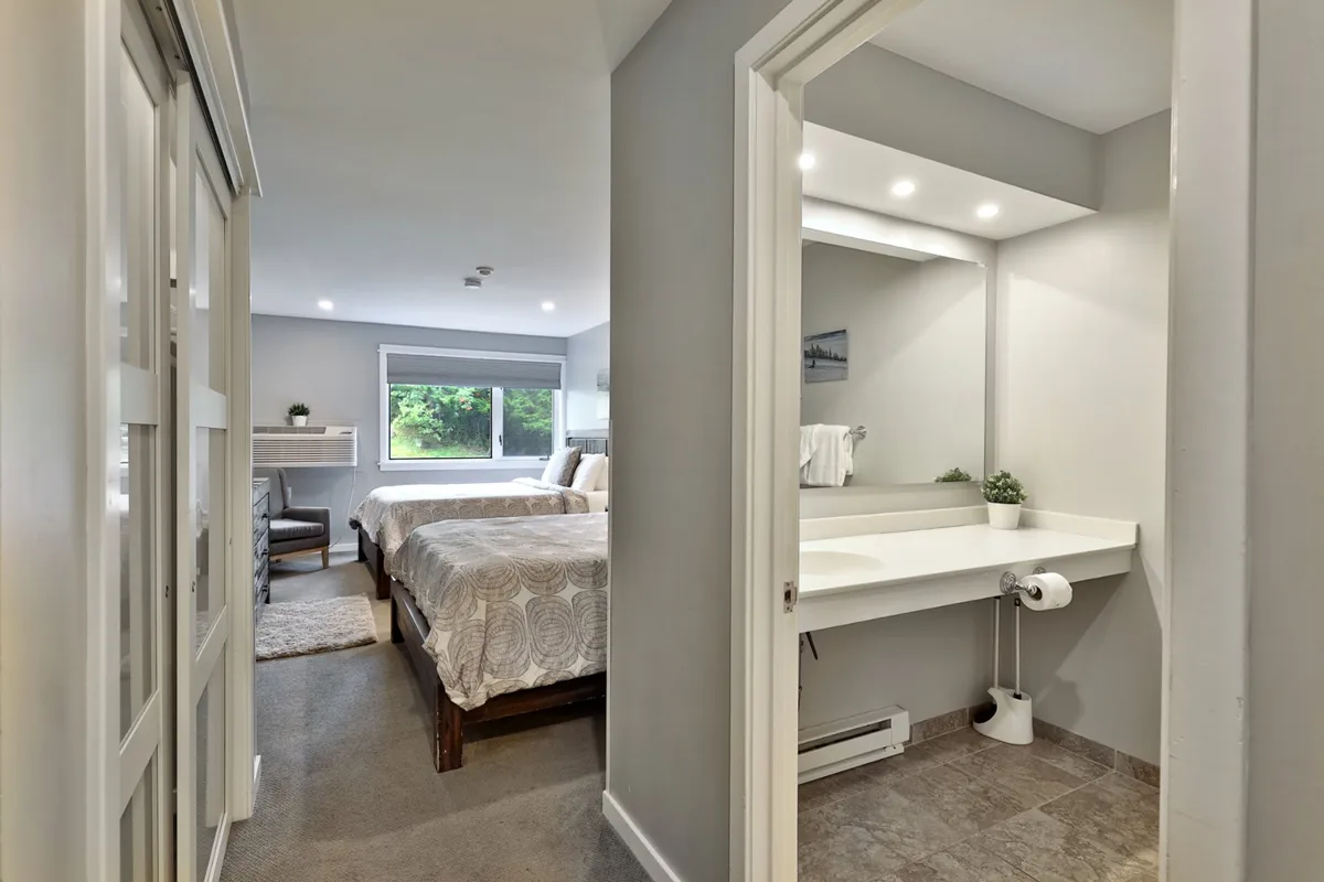 This image shows a comfortable studio layout featuring two beds, a vanity area, and a window framing lush greenery outside. The room is bathed in natural light, creating a welcoming and serene atmosphere ideal for families or groups.