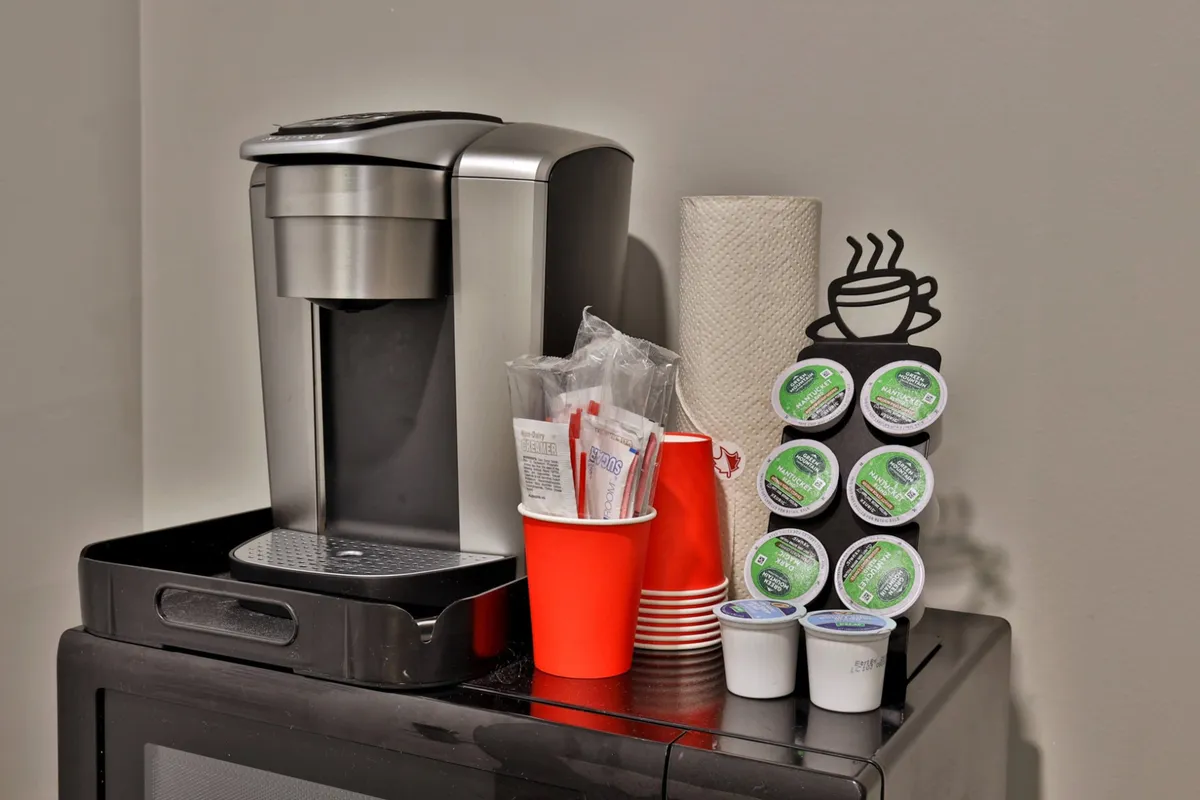 A kitchenette setup with a coffee maker, vibrant red cups, coffee pods, and paper towels—all arranged for easy access and spontaneity. The scene suggests a space for quick refreshments and social moments, enhancing the guest's experience.