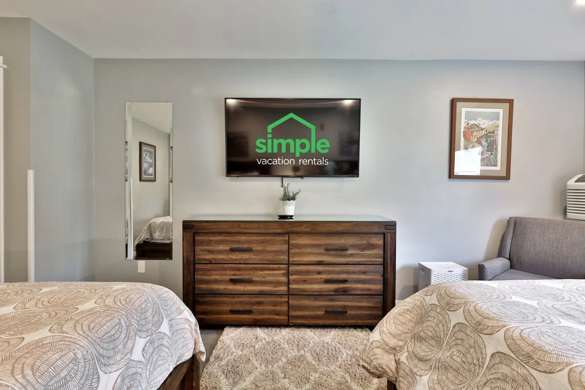 A stylish room with a television displaying the property's logo, a dresser, and a bedside table. The scene suggests modern amenities and a comfortable environment, ideal for unwinding after a day of adventure.